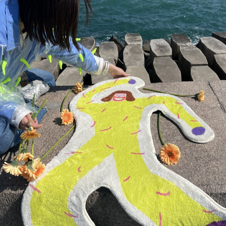 Person arranging flowers around a colorful artwork of a person on a stone pathway by the water.